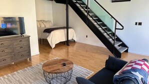 A modern living room with a sofa, a coffee table, a TV on a wooden cabinet, and a staircase leading to another level.