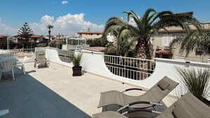A rooftop terrace with lounge chairs, a table, and potted plants.