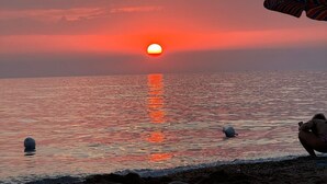 A sunset over a beach with a clear sky, calm sea, and a few boats.