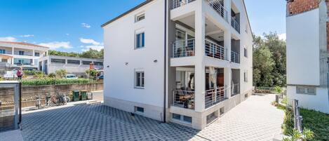 A modern two-story building with balconies, a paved courtyard, and a clear sky.