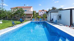 Ein Swimmingpool mit blauen Fliesen, umgeben von Liegestühlen und einem weißen Gebäude.