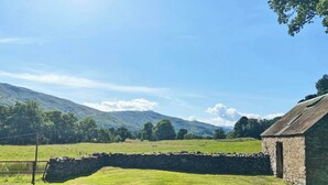 A stone wall, a grassy field, and a stone building with a sloped roof.