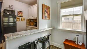 A kitchen with a refrigerator, microwave, and bar stools. There is a window with blinds and a painting on the wall. - < 1 Mi to Downtown Conroe: Charming Apartment (Conroe)