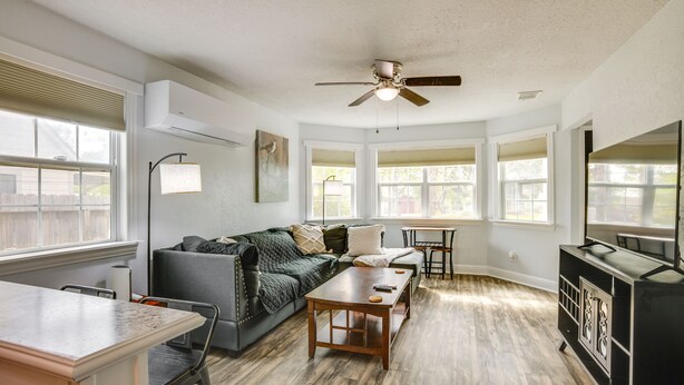 A living room with a sofa, coffee table, and dining area. There is a ceiling fan, windows, and a TV stand. - < 1 Mi to Downtown Conroe: Charming Apartment (Conroe)