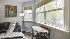 A room with a dark gray couch, a wooden table, and a large window with blinds. - < 1 Mi to Downtown Conroe: Charming Apartment (Conroe)