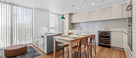 A modern kitchen with a dining area, wooden flooring, and a built-in wine cooler.