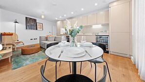 A modern living room with a dining area, a sofa, a coffee table, and a kitchen in the background. - SERCASA - Regents Park (London)