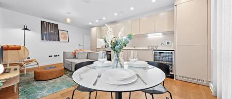 A modern living room with a dining area, a sofa, a coffee table, and a kitchen in the background.