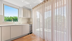 A modern kitchen with a large window, wooden flooring, and a view of greenery outside. - SERCASA - Regents Park (London)