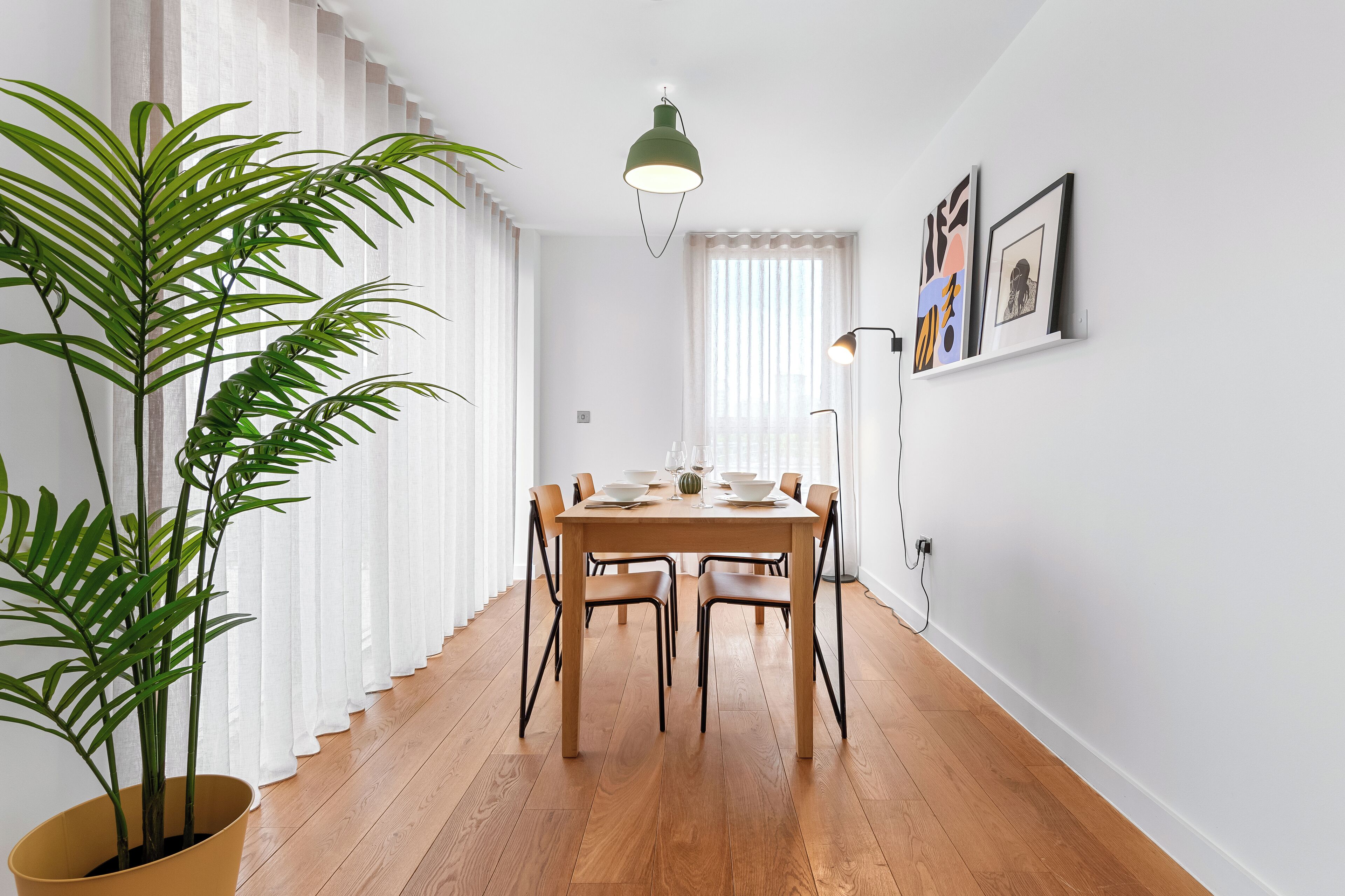 A dining area with a wooden table, chairs, a potted plant, and artwork on the wall.