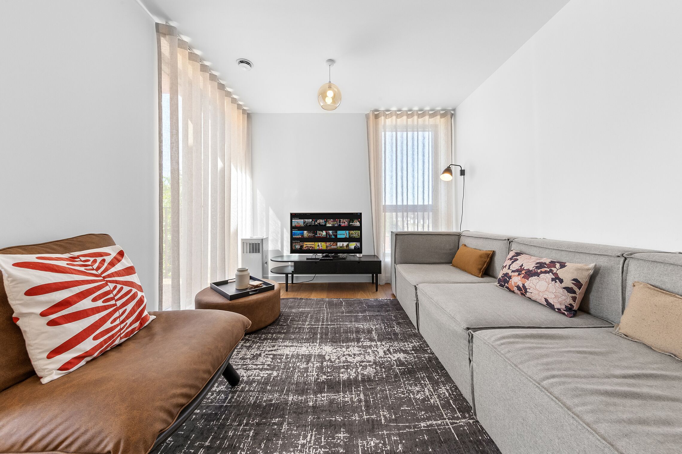 A modern living room with a brown sofa, grey sofa, and a black rug. There is a television on a black stand in the background.