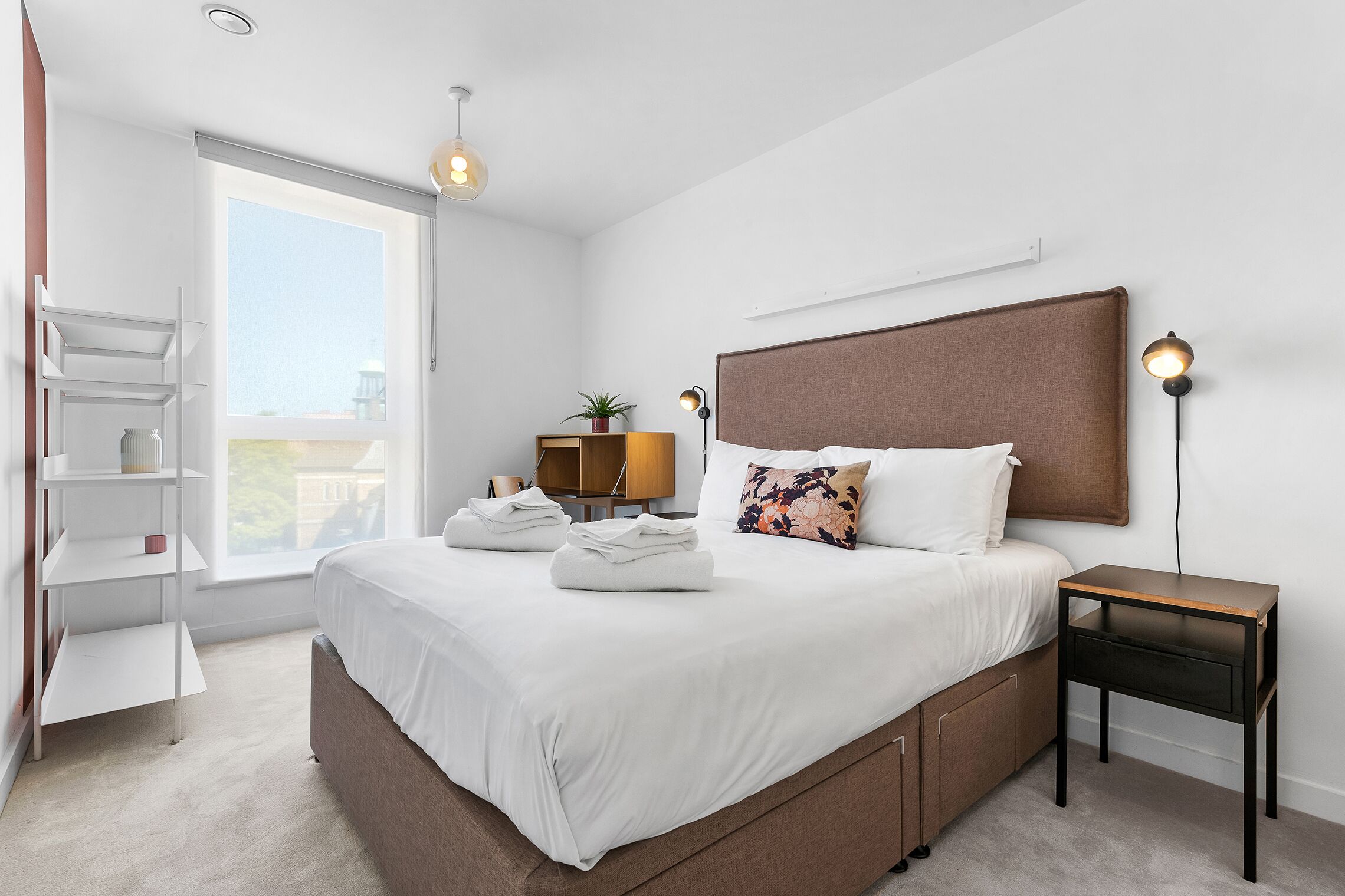 Un dormitorio moderno con una cama grande, mesitas de noche, una estantería y un ventanal con vistas.