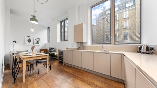 A modern kitchen with wooden flooring, a dining area with a table and chairs, and large windows with blinds. - SERCASA - Regents Park (London)