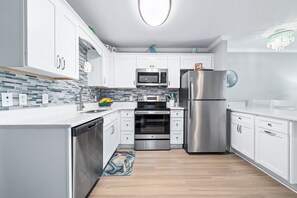 A modern kitchen with white cabinets, stainless steel appliances, a microwave, oven, and refrigerator.
