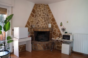 A kitchen with a stone fireplace, a white refrigerator, a microwave on a cart, and a potted plant. - Villa Dan  (Monopoli)
