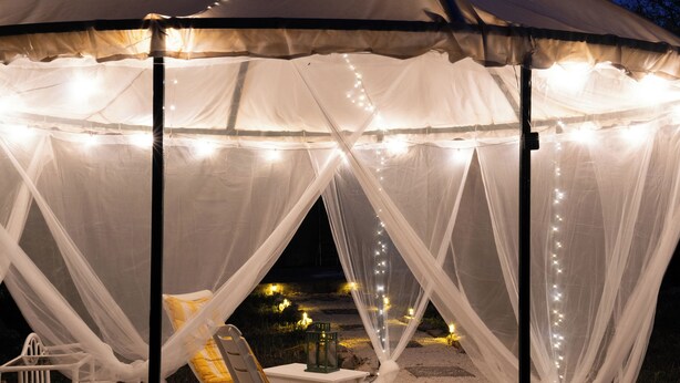 Una carpa con tela blanca y luces de cadena, una mesa y una silla.