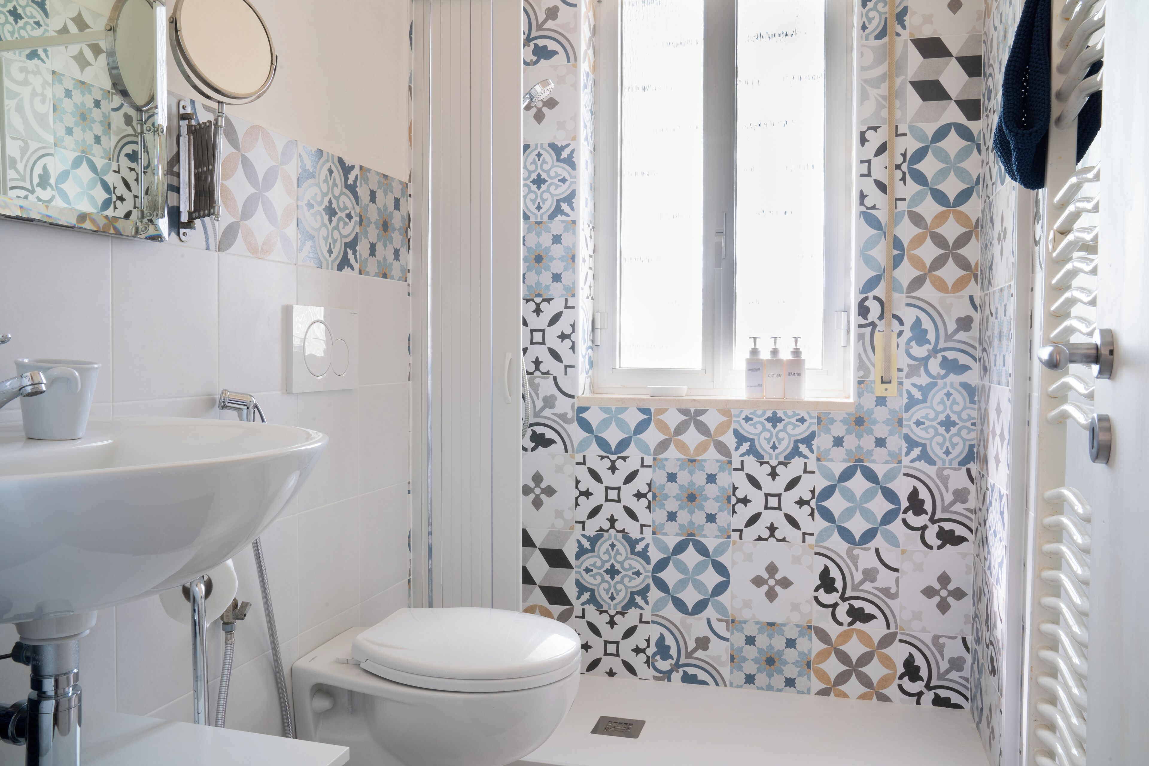 A bathroom with a white sink, toilet, and shower. The walls are tiled with geometric patterns.