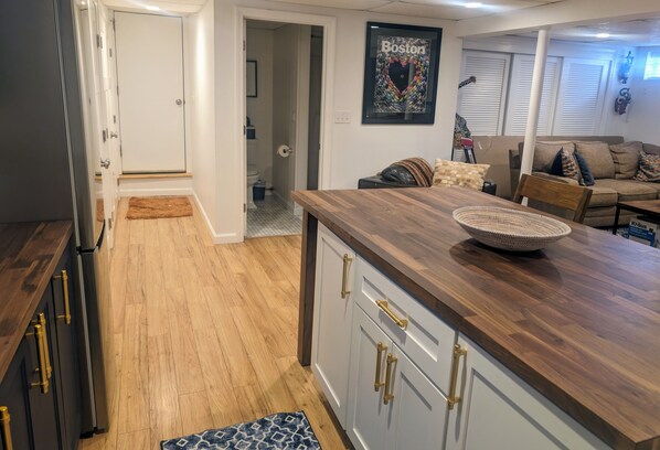 A modern kitchen with wooden cabinets and a large island, a living area with a sofa and cushions, and a framed 'Boston' sign on the wall.