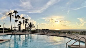 Une piscine dotée de chaises longues et bordée de palmiers, avec vue sur une étendue d’eau.
