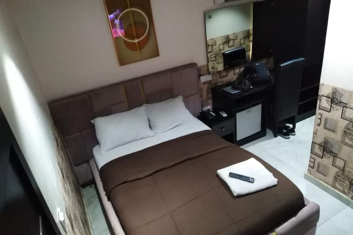 A neatly made bed with a brown blanket and a remote control on a white pillow.