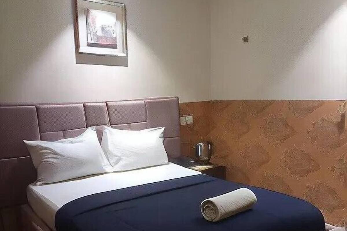A bed with a headboard, pillows, and a rolled towel.