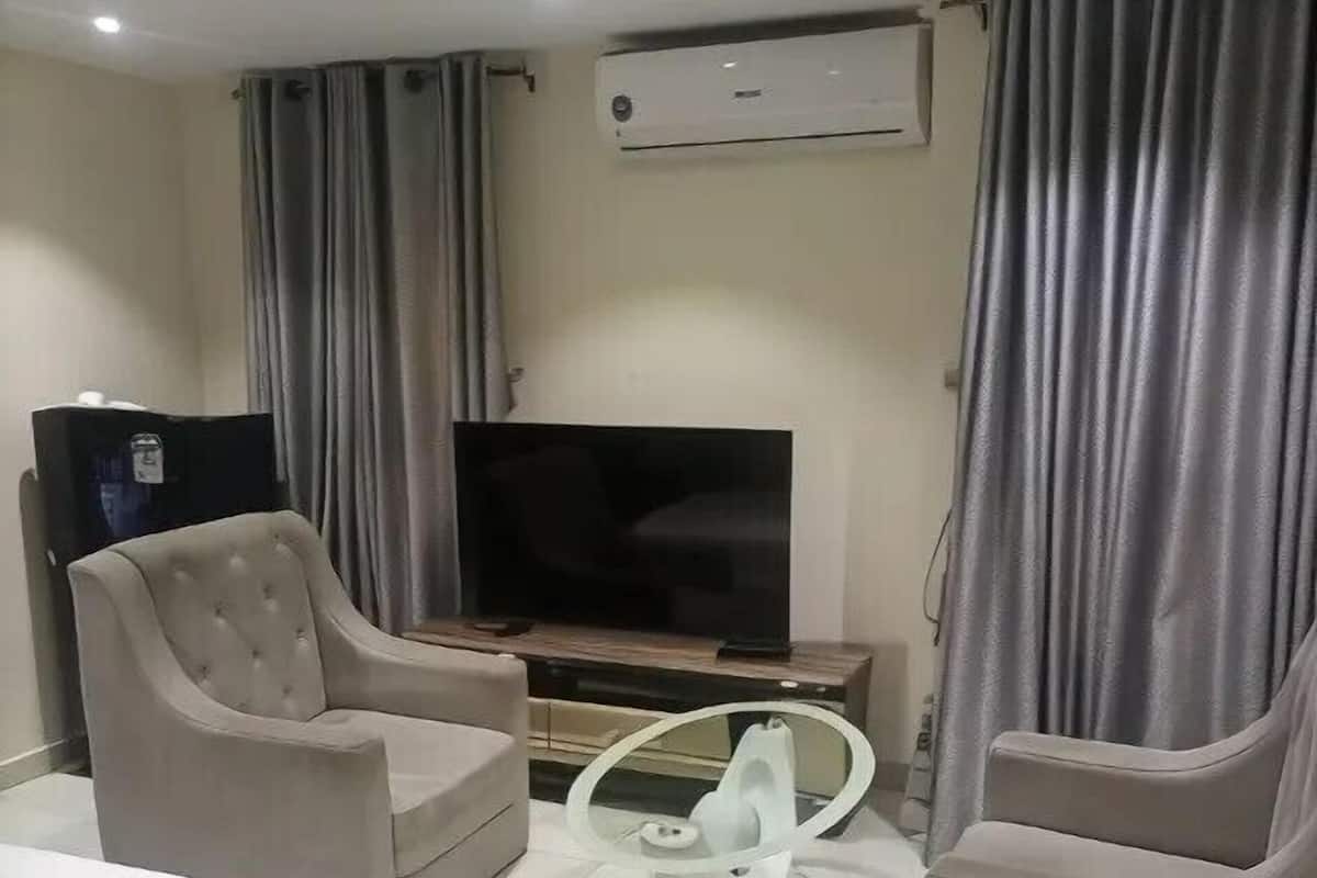 A modern hotel room with a bed, two armchairs, a TV, and an air conditioning unit.