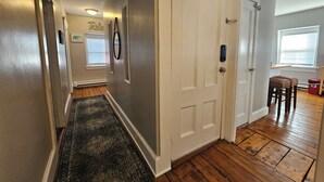 A hallway with a dark patterned rug, a white door, and a window with blinds. - Alice Pet-Friendly Downtown Newport Rental with Parking  (Newport)