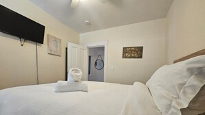 A neatly made bed with a rolled towel, a flat-screen TV mounted on the wall, a door, and a wall decoration. - Alice Pet-Friendly Downtown Newport Rental with Parking  (Newport)