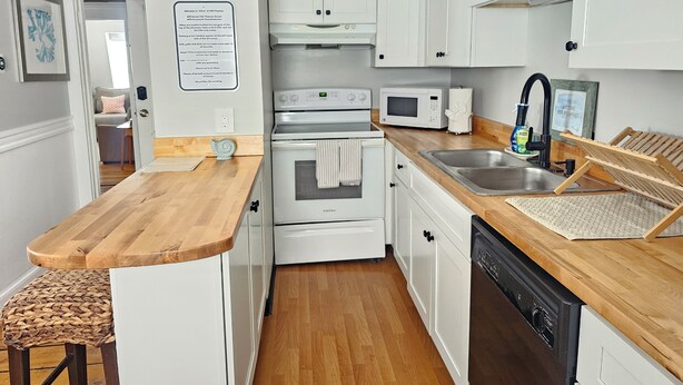 A compact kitchen with white cabinets, a wooden countertop, a built-in oven, a microwave, and a dishwasher. - Alice Pet-Friendly Downtown Newport Rental with Parking  (Newport)