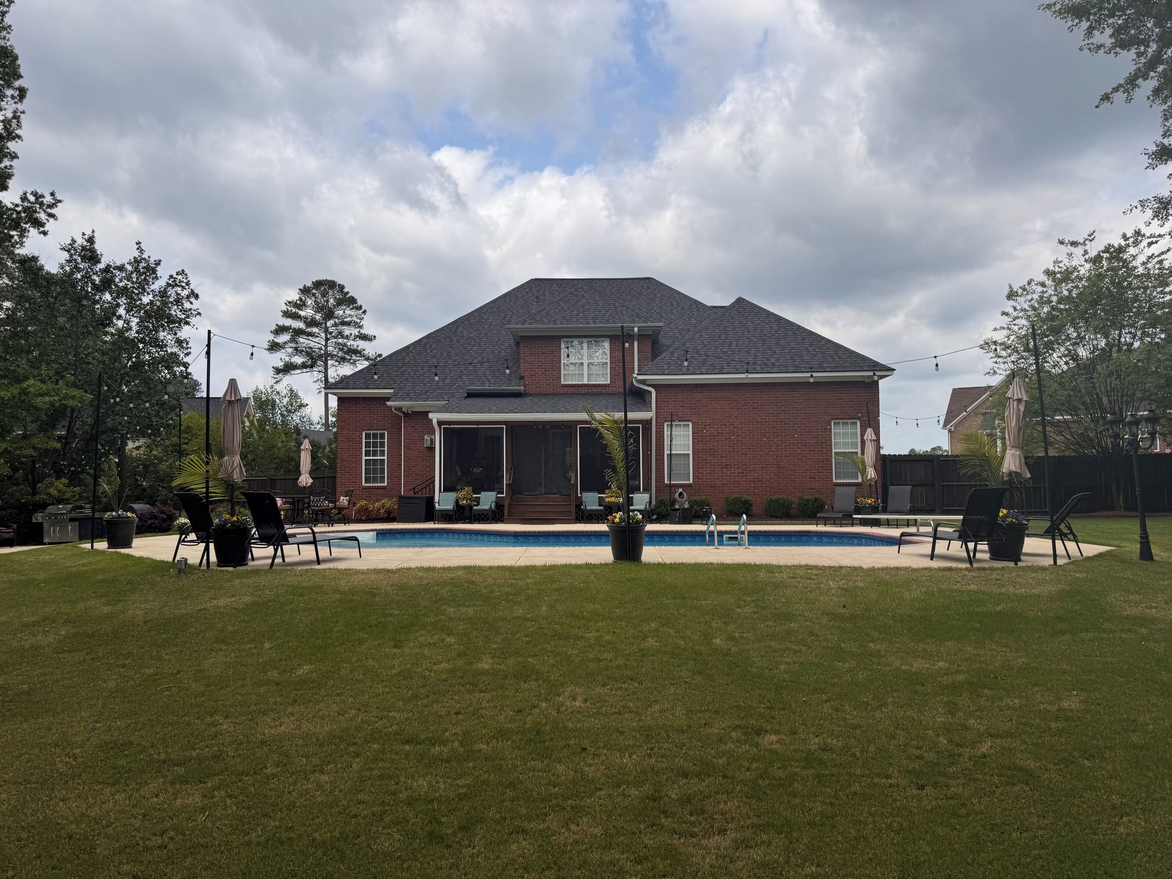 A two-story brick house with a covered patio, a swimming pool, and outdoor seating.