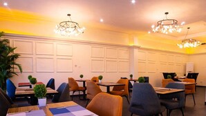 Un interior de restaurante con varias mesas y sillas, luces en el techo y una pared blanca con paneles.