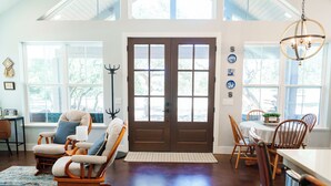 A spacious living room with a large window, a wooden rocking chair, a dining area with a table and chairs, and a chandelier. - Day Drippin’ Farmstay (Dripping Springs)