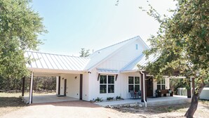A single-story house with a covered porch, a garage, and a small patio area. - Day Drippin’ Farmstay (Dripping Springs)