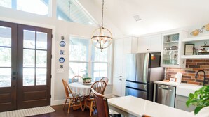 A modern kitchen with white cabinetry, a stainless steel refrigerator, and a dining area with wooden chairs and a white table. - Day Drippin’ Farmstay (Dripping Springs)