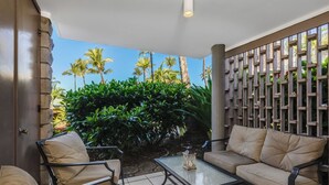 Un espace patio aménagé avec un canapé et des fauteuils, un sol carrelé et une vue sur des palmiers et une végétation luxuriante.