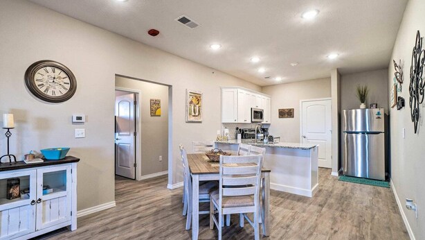A modern kitchen with white cabinets, stainless steel appliances, and a wooden dining table with chairs. - NEW Condo: No stairs, Arcade 🎮, Branson Skyline & Ozarks Views, 1GB WiFi! (Branson)