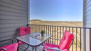 A balcony with a glass table and two pink chairs, overlooking a dry landscape with distant buildings. - NEW Condo: No stairs, Arcade 🎮, Branson Skyline & Ozarks Views, 1GB WiFi! (Branson)