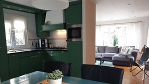 Een moderne keuken met groene kasten, een blauwe eettafel en een magnetron.