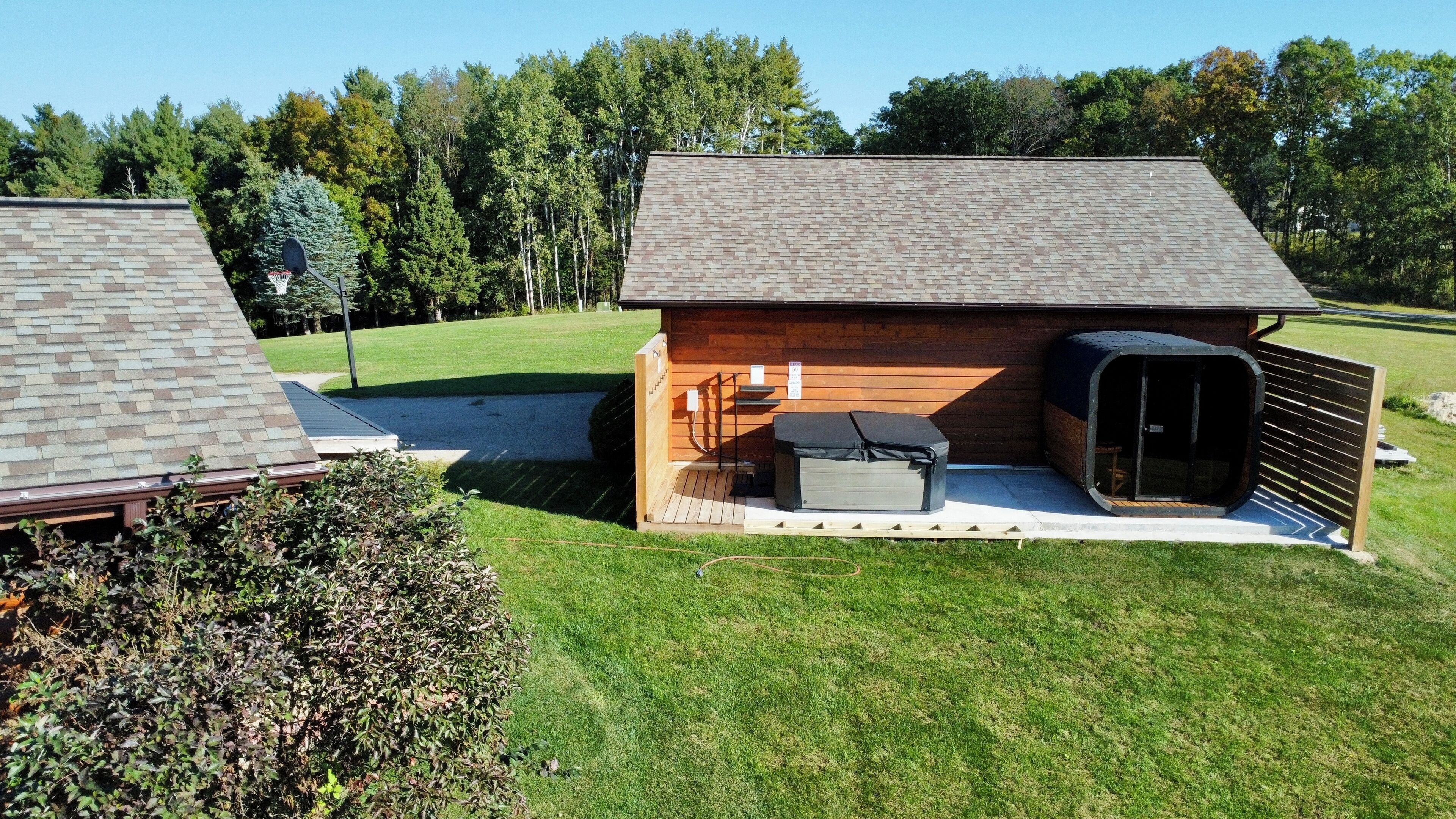 Eine kleine Holzhütte mit Terrasse, Grill und überdachter Sitzgruppe.