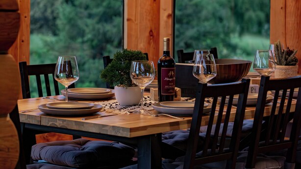 A wooden interior with a chandelier, dining table set with wine glasses, plates, and a potted plant. - Private Cabin Resort l Pool • Hot Tub • Sauna Wanderlust Cabin (Lodi)