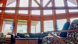 A spacious room with a high ceiling, wooden beams, large windows, a ceiling fan, and a seating area with a sofa and armchairs. - Private Cabin Resort l Pool • Hot Tub • Sauna Wanderlust Cabin (Lodi)