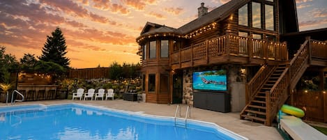A pool area with a wooden deck, lounge chairs, and a TV screen.