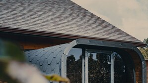 Une cabane en bois dotée d’un toit en pente et d’une grande porte vitrée donnant sur un espace extérieur aménagé pour s’asseoir.