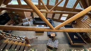 A log cabin interior with a loft bedroom, a living area with a sofa and coffee table, and a view of the forest through large windows. - Private Cabin Resort l Pool • Hot Tub • Sauna Wanderlust Cabin (Lodi)