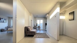 Un pasillo moderno con un sofá y sillones, una alfombra y un área de comedor al fondo.