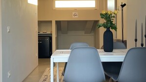 Un comedor moderno con una mesa blanca, sillas grises, un florero con flores amarillas y una cocina al fondo.