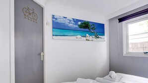 Una camera da letto con un letto, un quadro raffigurante una spiaggia, una porta e una finestra con tende.