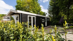 Un piccolo chalet moderno con una porta scorrevole in vetro, immerso nel verde e circondato da alberi.