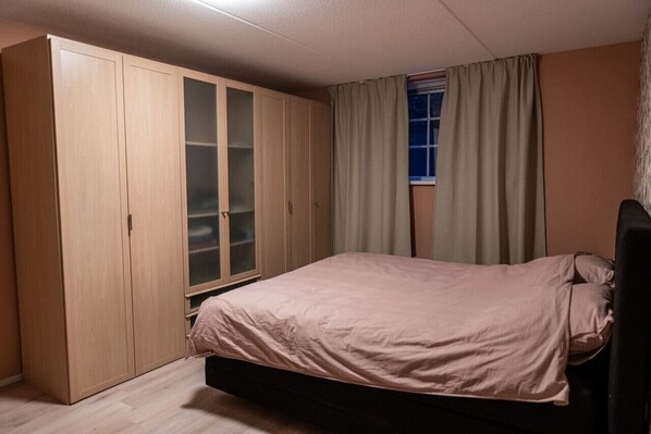 A bedroom with a bed, a wardrobe, and a window with curtains.