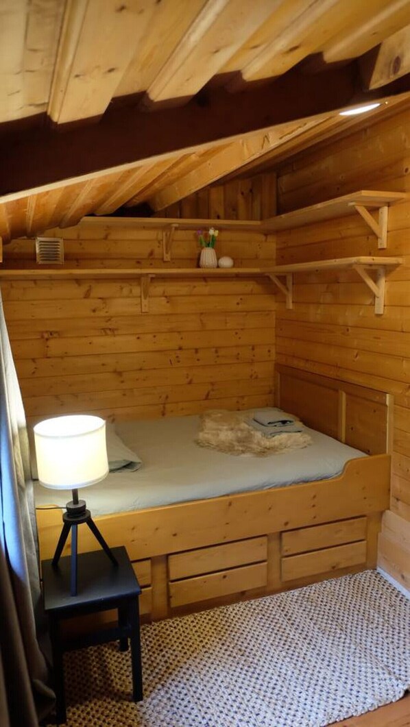 A small, cozy room with a bunk bed, a bedside table with a lamp, and a shelf with a vase and a small plant.